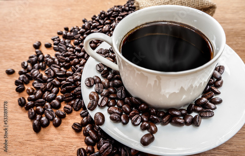 Cup of coffee with roasted beans on wood background