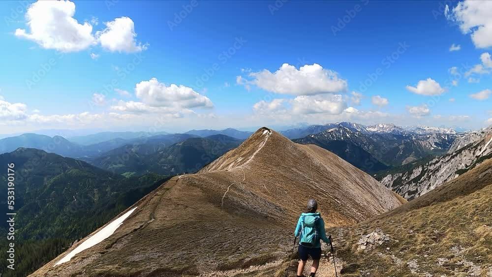 Rear view of active woman with backpack walking on ridges. Panoramic view of snow capped mountain peaks in Hochschwab Alps, Upper Styria, Austria, Europe. Hiking trail to Foelzstein, Foelzkogel Rear view of active woman with backpack walking on ridges. Panoramic view of snow capped mountain peaks in Hochschwab Alps, Upper Styria, Austria, Europe. Hiking trail to Foelzstein, Foelzkogel