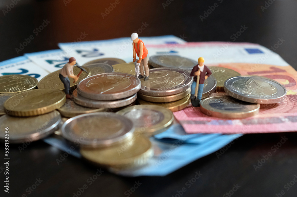 Miniature figurines of worker working on a pile of money Miniature figurines of worker working on a pile of money