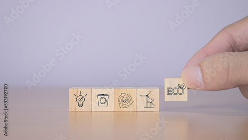 Hand puts wooden cubes with clean energy icon standing on eco friendly icon.Save of earth, saving environment, net zero emissions concept. Green business and sustainable development. World earth day.