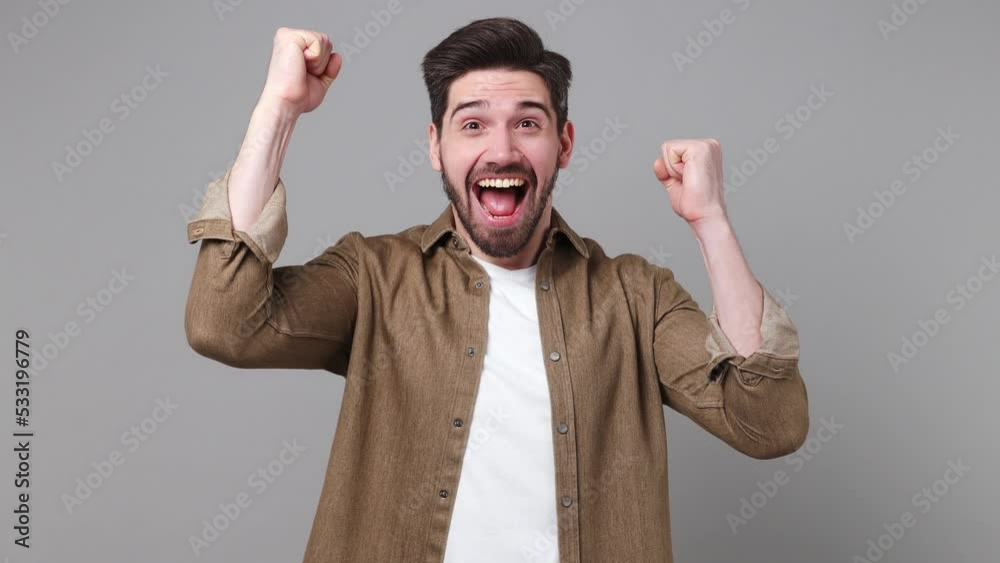Young excited jubilant overjoyed happy man 20s he wear brown shirt doing winner gesture celebrate clenching fists say yes isolated on plain grey background studio portrait. People lifestyle concept Young excited jubilant overjoyed happy man 20s he wear brown shirt doing winner gesture celebrate clenching fists say yes isolated on plain grey background studio portrait. People lifestyle concept