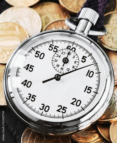 Analog stopwatch and pile of gold coins on a black background close-up. Counting time by stopwatch. Time measurement. Time management concept.A tool for measuring time.Dial stopwatch arrow