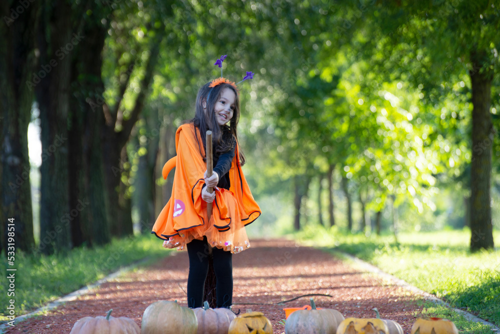 Obraz premium Child girl als little cute witch with pumpkin outdoors in halloween