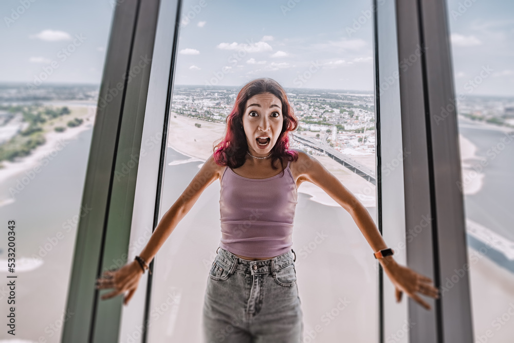 A girl with a phobia and fear of heights screams and reacts emotionally on the observation deck of the TV tower. Psychological challenge - obrazy, fototapety, plakaty 