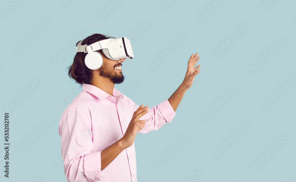 Overjoyed millennial guy isolated on blue studio background wear VR glasses explore new digital reality. Smiling young man in virtual reality headwear device have fun enjoy modern technologies.