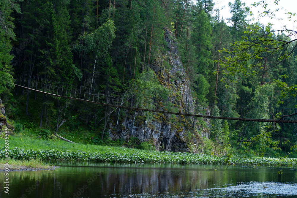 Suspended wooden bridge on the background of green trees and a river Suspended wooden bridge on the background of green trees and a river