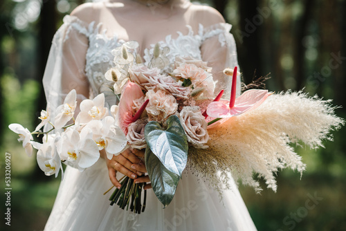 The bride in a white dress holds a wedding big vintage bouquet. The bouquet with white, pink flowers, roses, calla and decorative plants, leaves. Wedding day. A beautiful bride portrait in the forest.