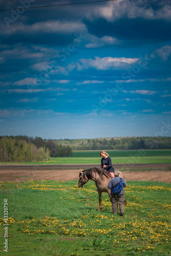 A young beautiful blonde girl trains a horse in the field.