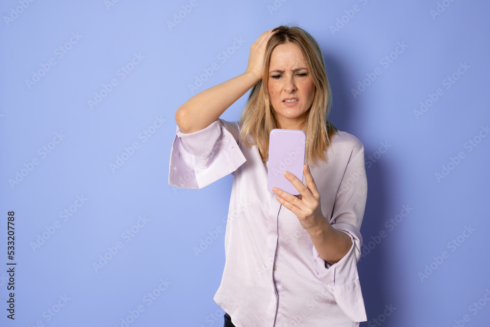 Upset woman holding a cellphone. Angry young businesswoman reading bad news on her cell phone. Isolated on purple background. Upset woman holding a cellphone. Angry young businesswoman reading bad news on her cell phone. Isolated on purple background.