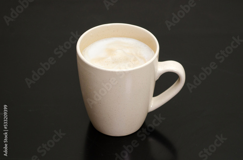 Fresh hot coffee latte or cappuccino in a white mug, with white foam, on a black background