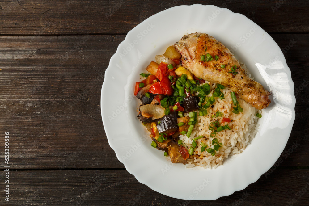 Rice with vegetables in sauce and chicken leg in a white plate on a wooden table.copy space Rice with vegetables in sauce and chicken leg in a white plate on a wooden table.copy space