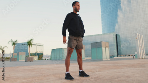 Young bearded male athlete doing workout  squats and jumping on the waterfront