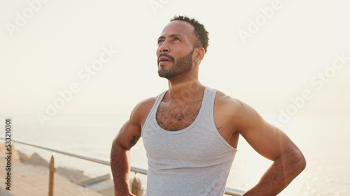 Young bearded male fit athlete standing on the embankment on the sea background