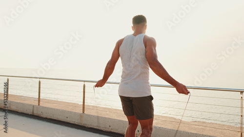 Young bearded male fit athlete jumping rope on the embankment