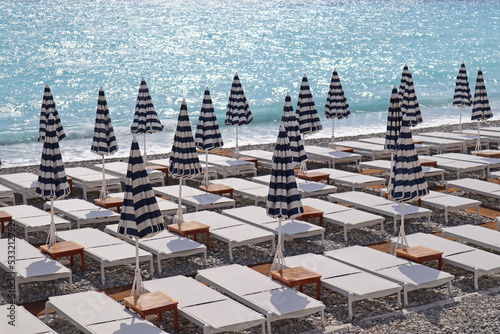 View of the beach with sun loungers and closed sun umbrellas in Nice  on the Mediterranean coast.