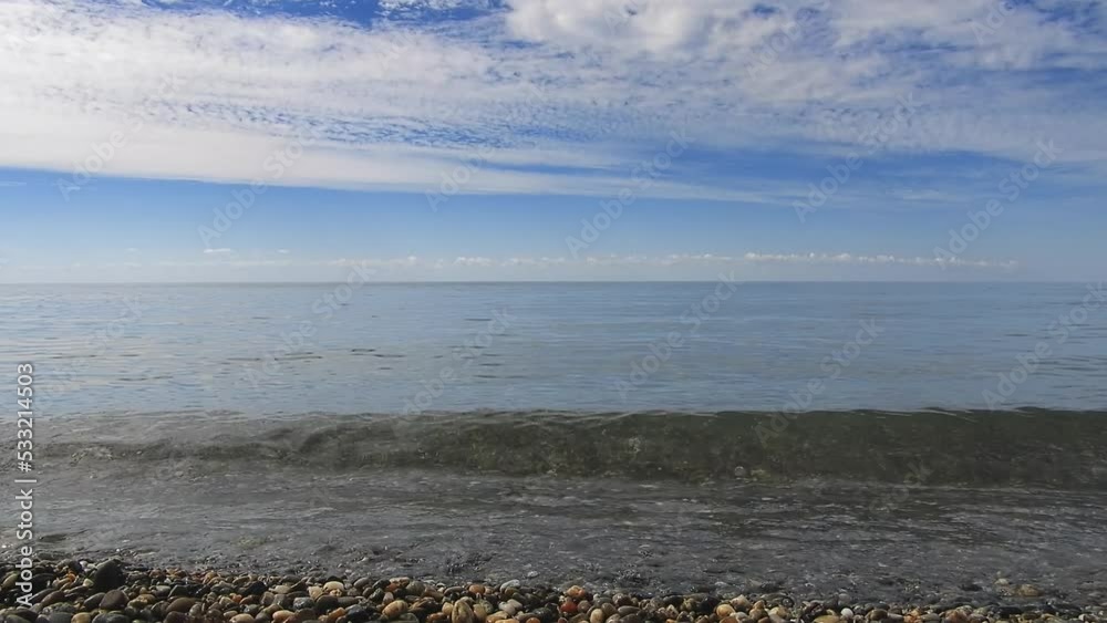 almost complete calm, a lazy Black Sea wave splashes on a pebble beach, cirrus clouds herald a change in the weather on a sunny summer morning almost complete calm, a lazy Black Sea wave splashes on a pebble beach, cirrus clouds herald a change in the weather on a sunny summer morning