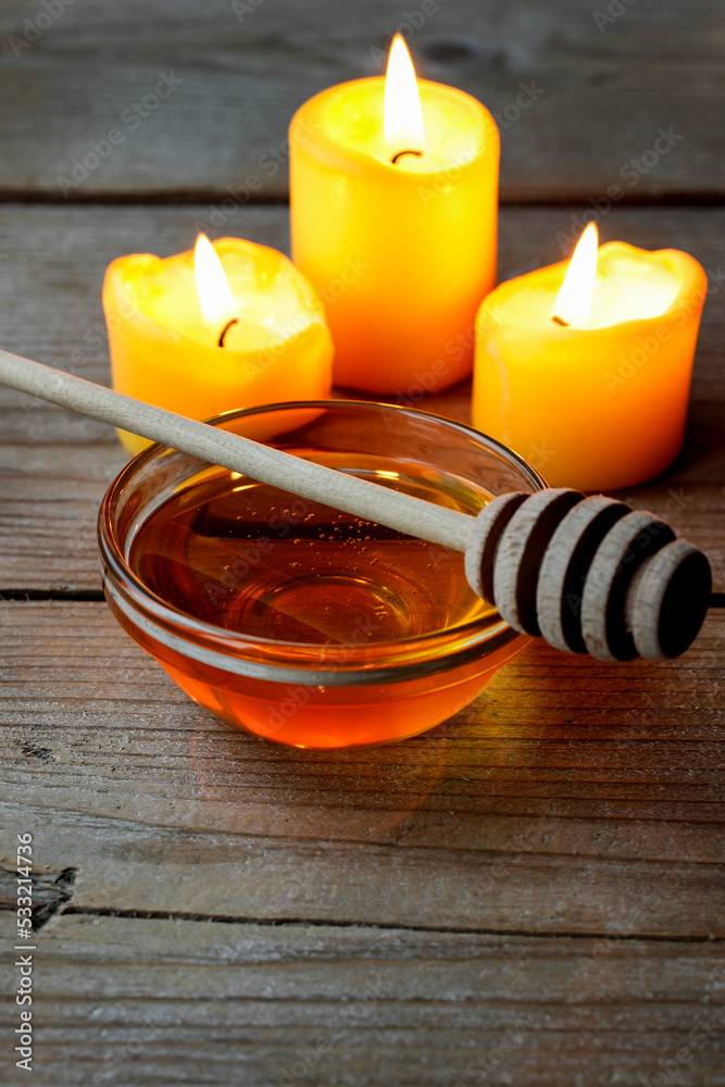 Bowl with honey and yellow candles on wooden table. Bowl with honey and yellow candles on wooden table.