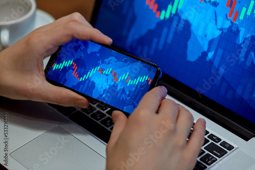 Trading. Businessman investor analyst using mobile phone analytics to analyze cryptocurrency financial market, trade data index chart graph on smartphone and laptop screen. close up