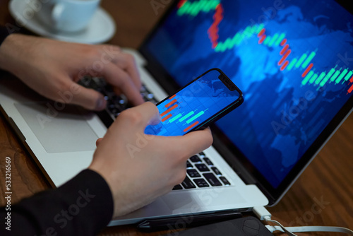 Trading. Businessman investor analyst using mobile phone analytics to analyze cryptocurrency financial market, trade data index chart graph on smartphone and laptop screen. close up