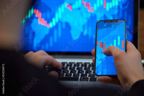 Trading. Businessman investor analyst using mobile phone analytics to analyze cryptocurrency financial market, trade data index chart graph on smartphone and laptop screen. close up