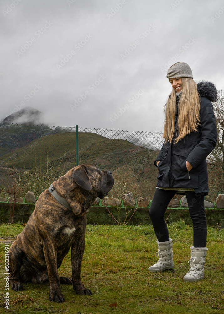 Young woman with long blonde hair and coat with her friend mastiff in the nature Young woman with long blonde hair and coat with her friend mastiff in the nature