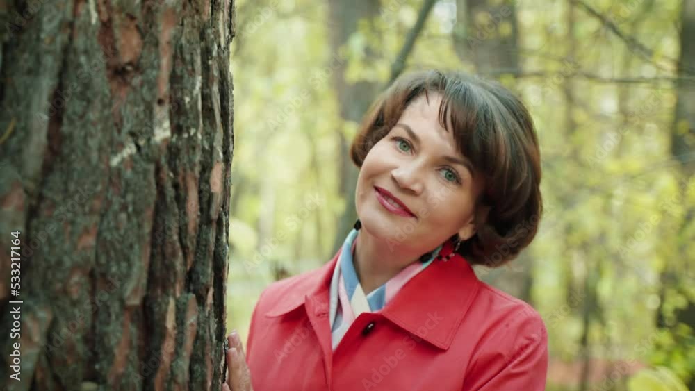 A beautiful woman in a red raincoat walks in the autumn park. A slender brunette hides behind a tree. Golden autumn and beautiful weather. Yellow foliage on the trees. A beautiful autumn day. Slow mot A beautiful woman in a red raincoat walks in the autumn park. A slender brunette hides behind a tree. Golden autumn and beautiful weather. Yellow foliage on the trees. A beautiful autumn day. Slow mot