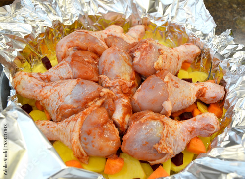 chopped raw vegetables and chicken drumsticks are stacked in foil and a baking dish. dietary, tasty dish for lunch or dinner. the concept of proper and healthy nutrition