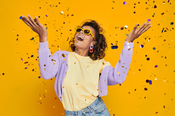 Beautiful African woman throwing confetti and smiling against yellow background