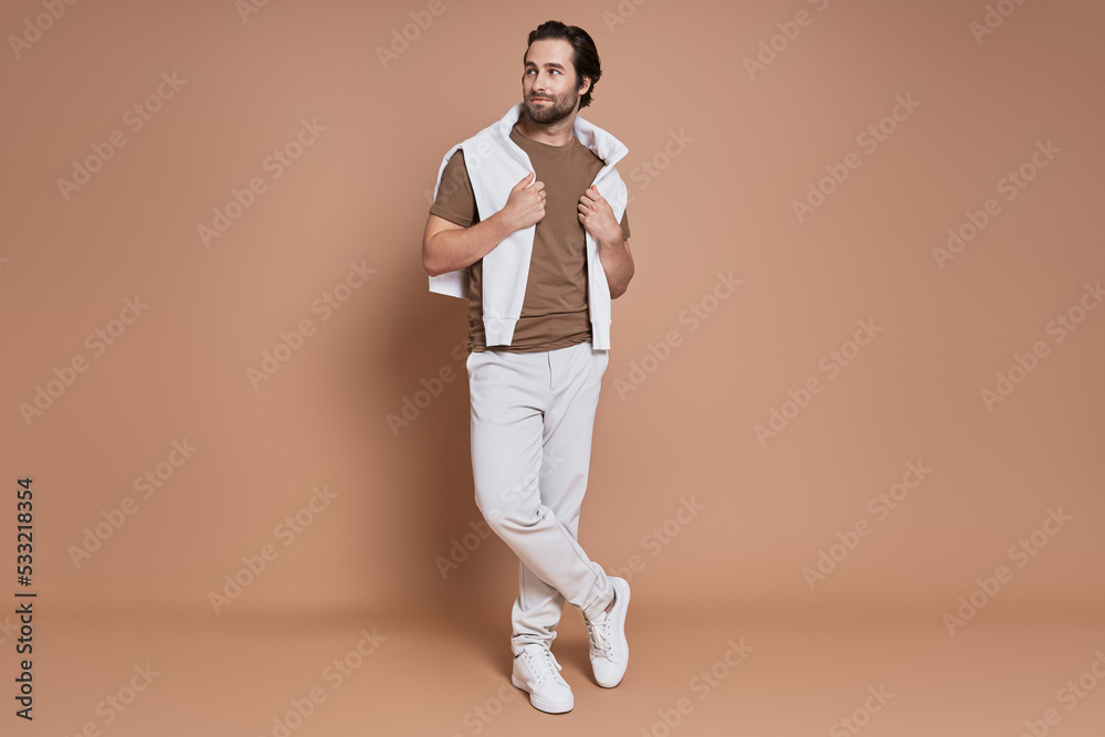 Full length of fashionable young man standing against brown background Full length of fashionable young man standing against brown background