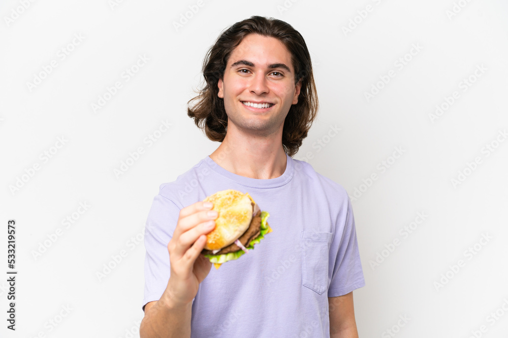 Young handsome man holding a burger isolated on white background with happy expression Young handsome man holding a burger isolated on white background with happy expression