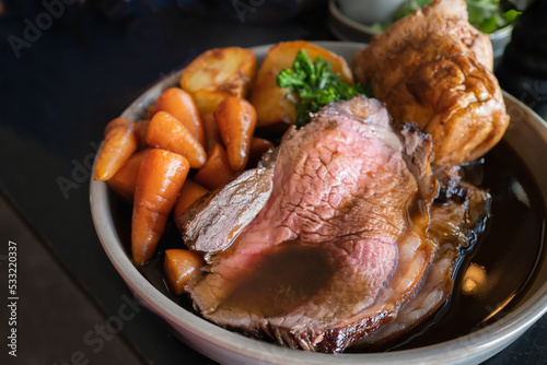 Roast beef slices on a plate with carrots, roast potatoes, a Yorkshire pudding and gravy, making a complete Sunday roast meal. photo