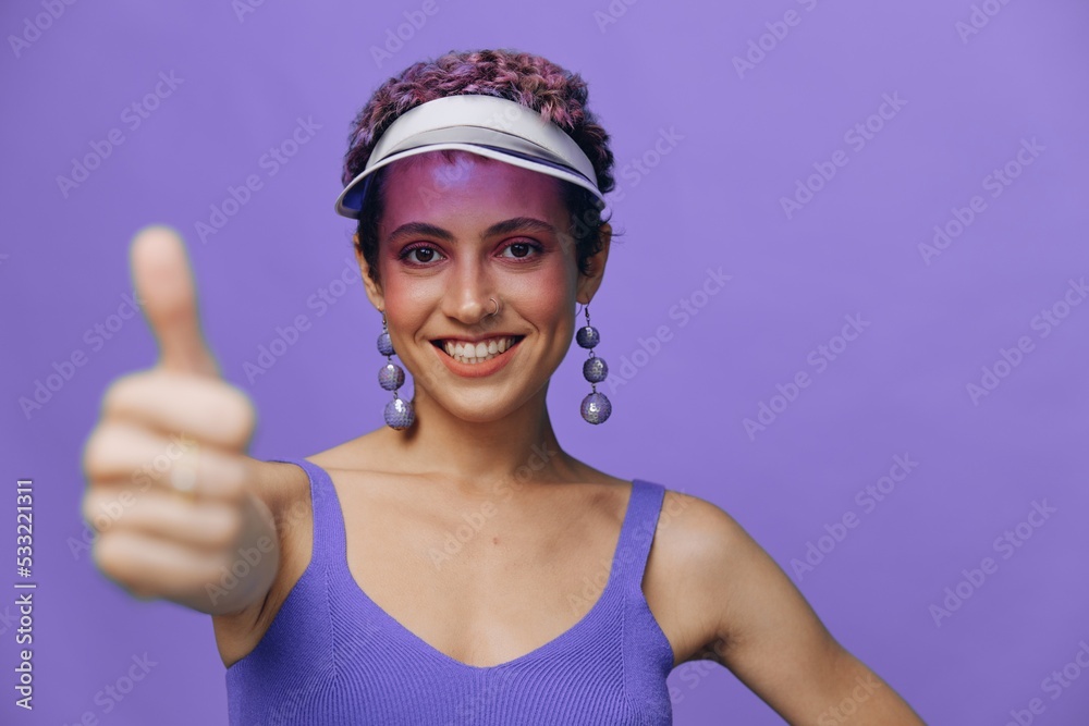 Portrait of a sporty fashion woman posing smiling with teeth and pointing a finger at the camera in a purple yoga tracksuit and a transparent cap on a purple monochrome background Portrait of a sporty fashion woman posing smiling with teeth and pointing a finger at the camera in a purple yoga tracksuit and a transparent cap on a purple monochrome background