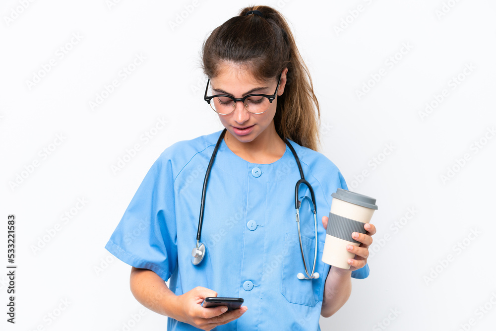 Young nurse doctor woman isolated on white background holding coffee to take away and a mobile Young nurse doctor woman isolated on white background holding coffee to take away and a mobile