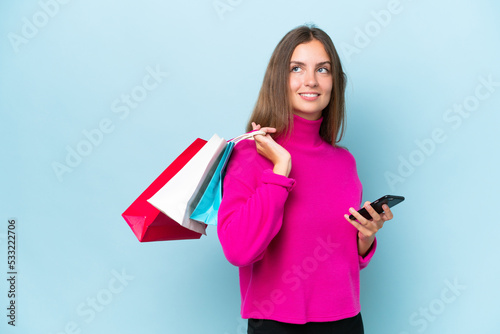 Young beautiful woman isolated on blue background holding shopping bags and a mobile phone