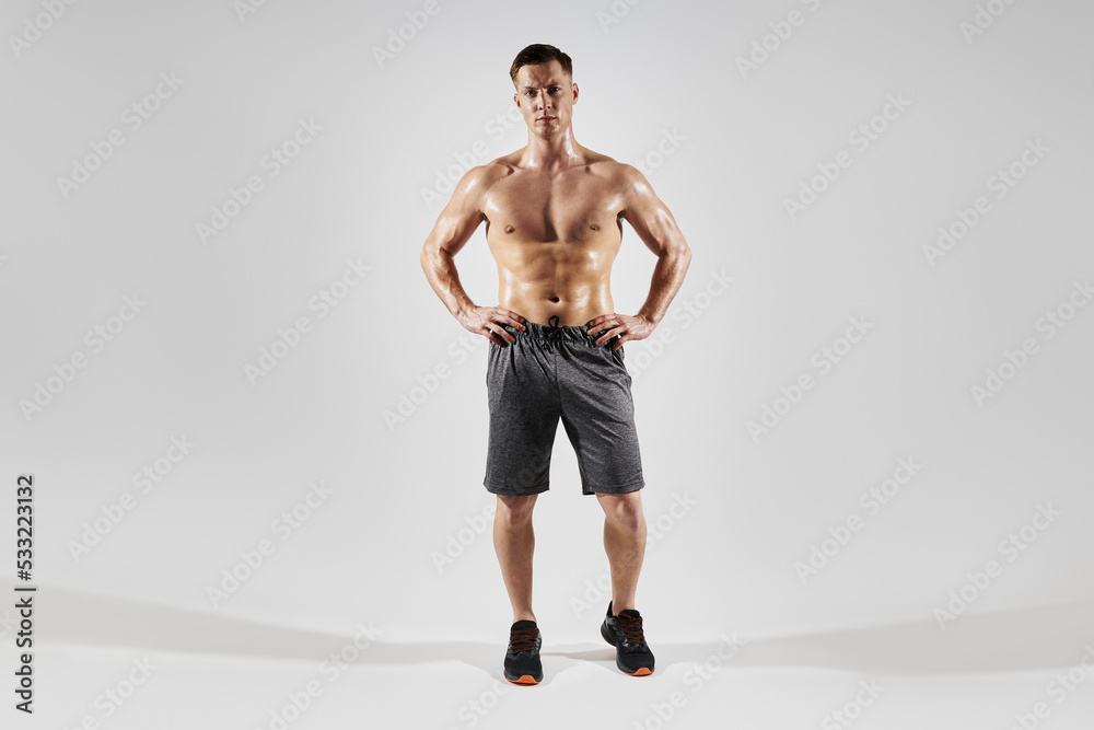 Handsome muscular man holding hands on hip while standing against white background