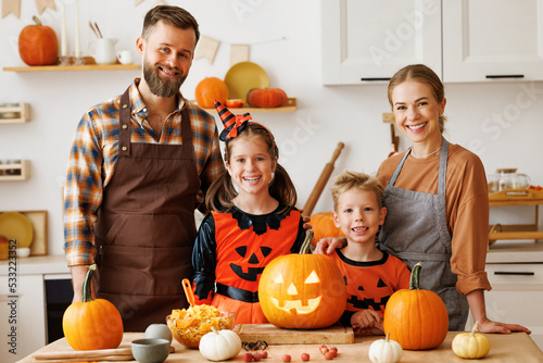 Happy family mother, father and kids  looking at camera while  make jack-o-lantern from pumpkin, getting ready for halloween photo