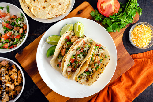 Chicken Tacos Topped with Pico de Gallo and Cheese: Three tacos on a plate surrounded with toppings and tortillas