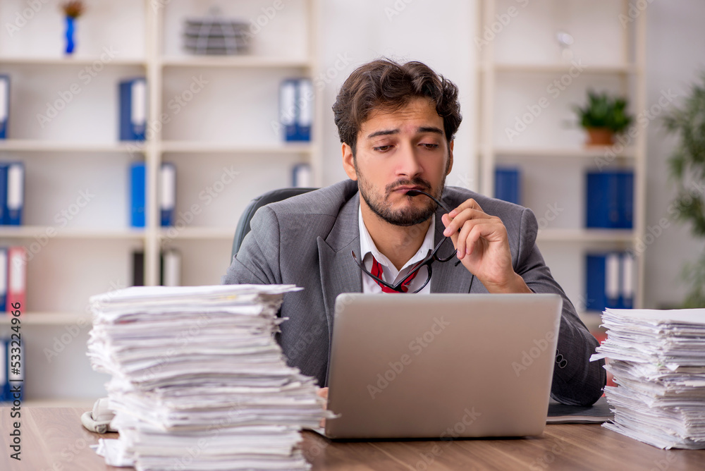Young male employee unhappy with excessive work in the office Young male employee unhappy with excessive work in the office