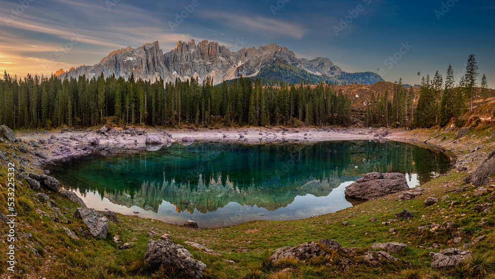 Carezza, Italy - Panoramic view of Lake Carezza (Lago di Carezza) with the Italian Dolomites reflecting on the lake. Warm autumn sunrise with colorful sky in South Tyrol