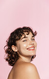Skin care. Woman with beauty face and healthy facial skin portrait. Beautiful curly girl model with natural makeup touching glowing hydrated skin on pink background closeup. High quality image