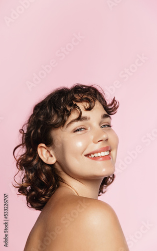 Skin care. Woman with beauty face and healthy facial skin portrait. Beautiful curly girl model with natural makeup touching glowing hydrated skin on pink background closeup. High quality image