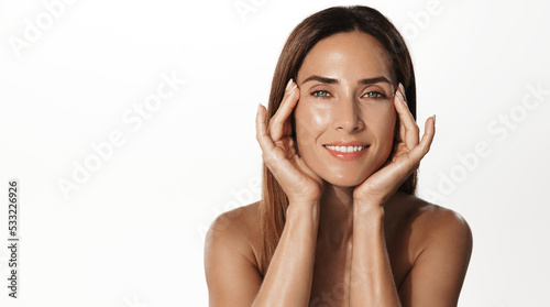 Portrait of smiling middle-aged woman using anti-aging cream, skincare treatment from wrinkles, has clear nourished skin, white background