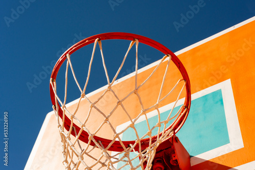 Colourful orange basketball backboard with red hoop and a net against blue sky low angle view. photo