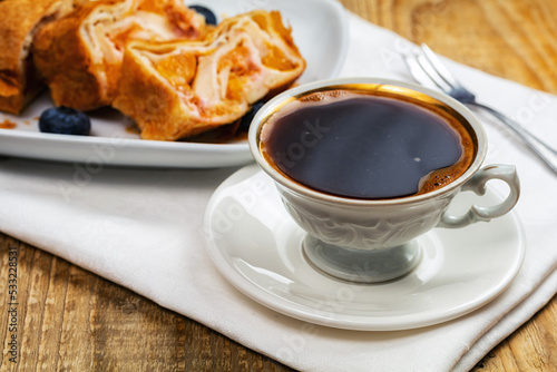 cup of coffee and piece of apple strudel on wooden table.