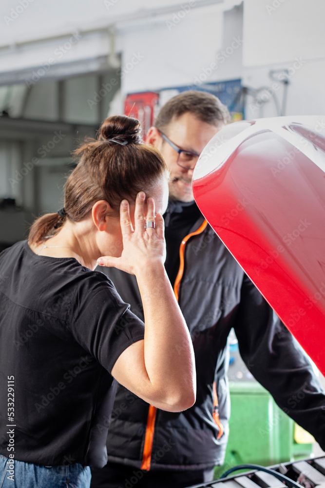 Obraz premium Car repair in the workshop. The mechanic shows the client a fault under the hood.
