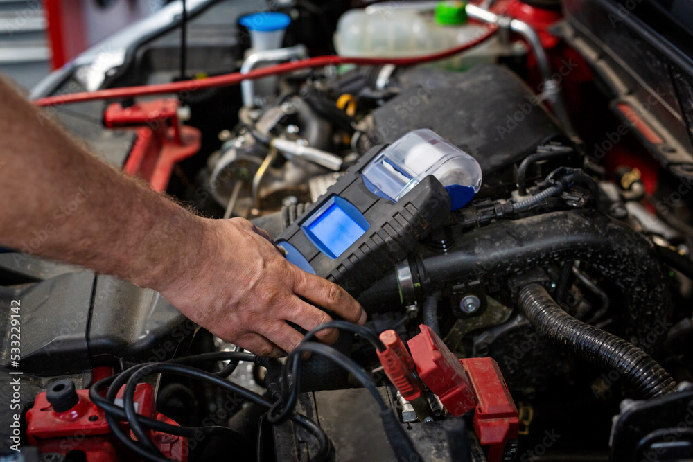 Checking the voltage in the battery. An electrician connects a meter in a car repair shop.