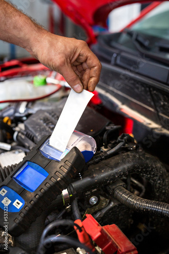 Measure the battery voltage with a meter. A mechanic checks the battery with a meter in a car workshop.