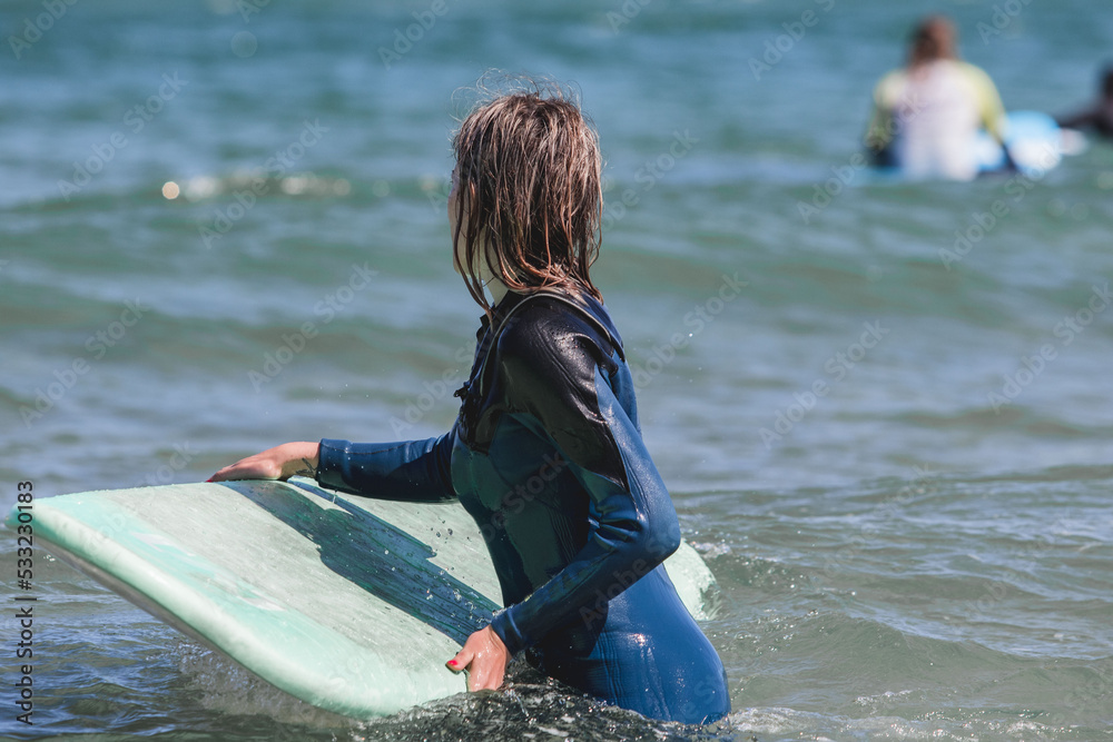 Obraz premium young surfer in the water with his board waiting for the waves during a surf and travel week experience in Somo, Cantabria (Spain)
