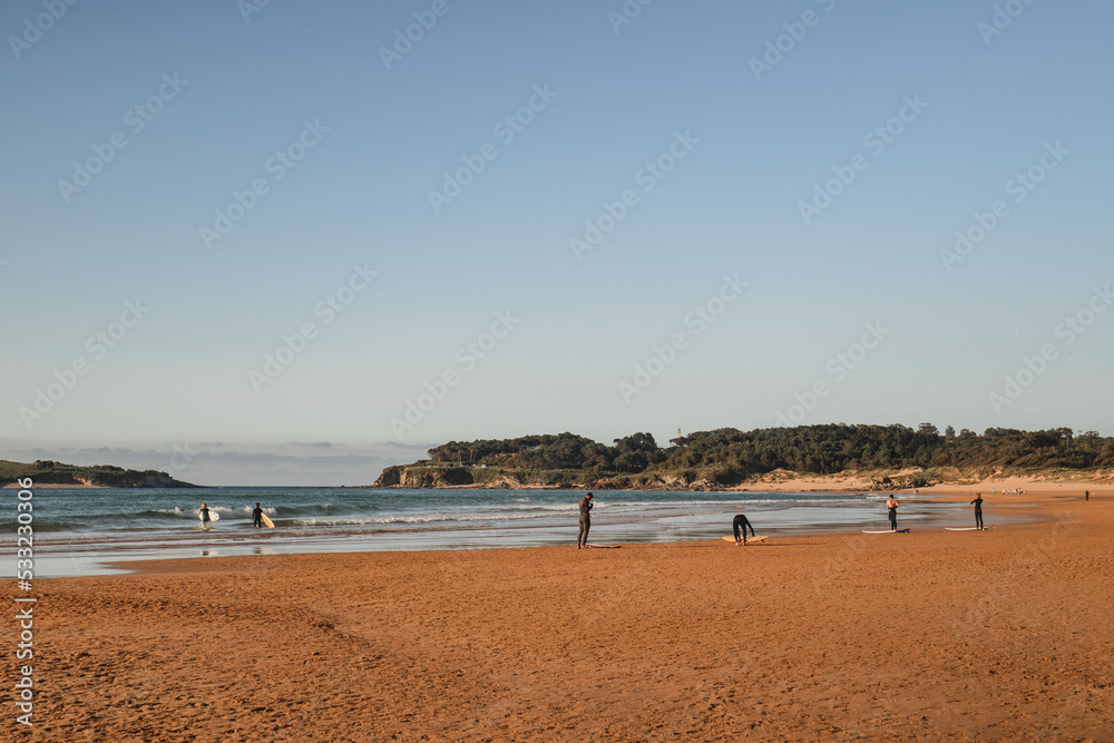 group of surfers on the beach as they prepare to enter the water for surfing during a surf and travel week experience in Somo, Cantabria (Spain)
