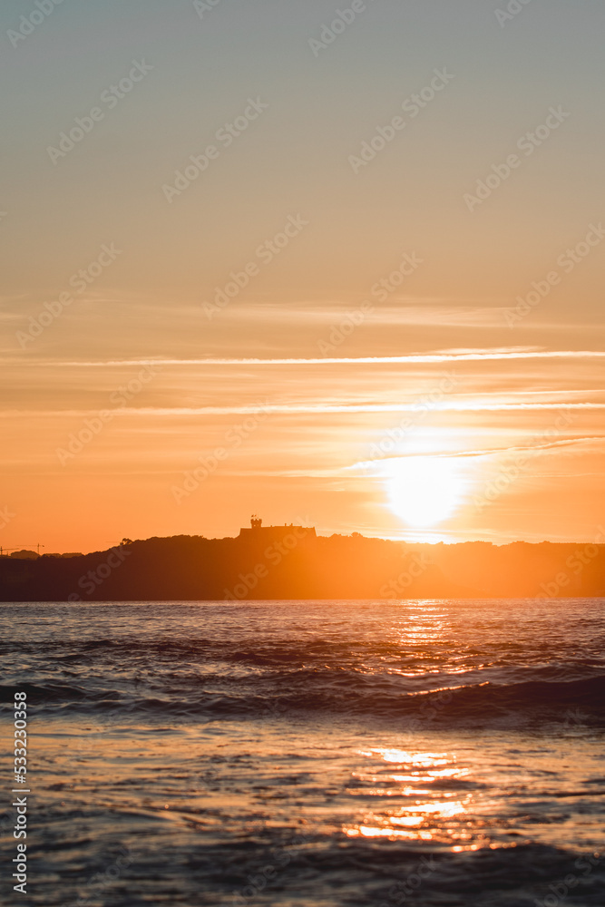 Obraz premium Spectacular panoramic view of a castle on the horizon on the mountain over the sea at sunset during a surf and travel week experience in Somo, Cantabria (Spain)